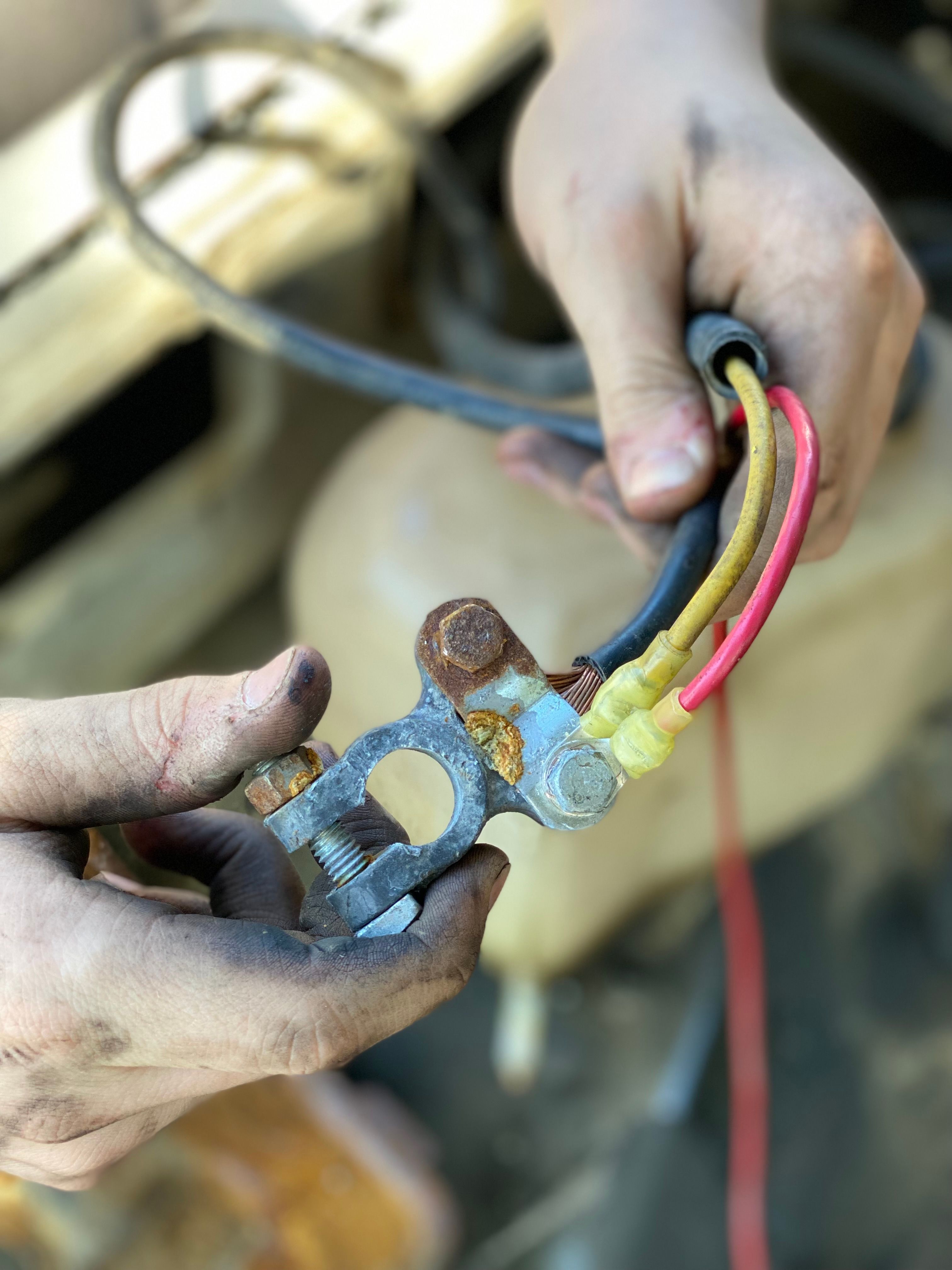 Hands working on a car battery terminal and wiring during repair
